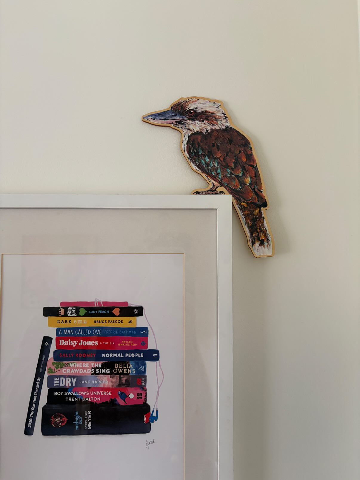 Wooden kookaburra door topper sitting on a framed illustration of books.